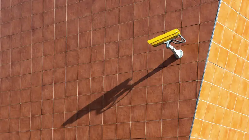 Caméra de surveillance jaune fixée en hauteur sur un mur orangé