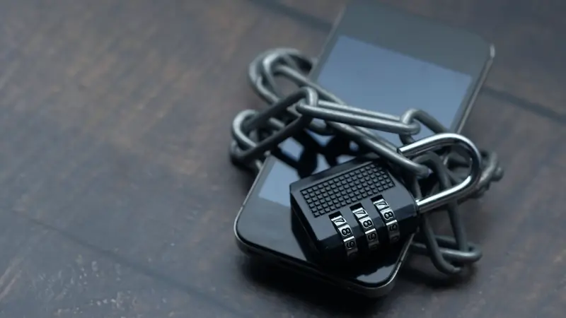 Smartphone posé sur une table en bois, entouré d'une chaîne fermée par un cadenas à code