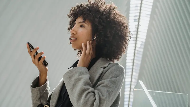 Femme aux cheveux bouclés parlant à son smartphone tenu devant elle, un écouteur sans fil à l'oreille