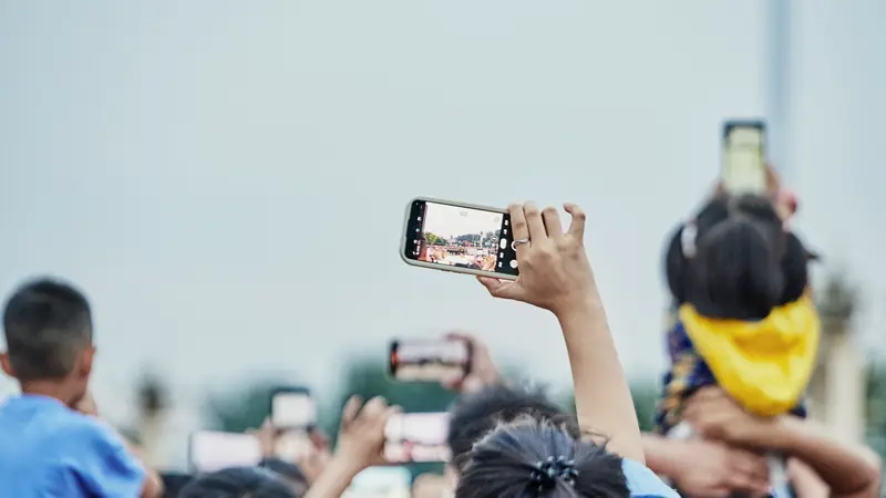 Main levée tenant un smartphone qui photographie une scène au milieu d'une foule