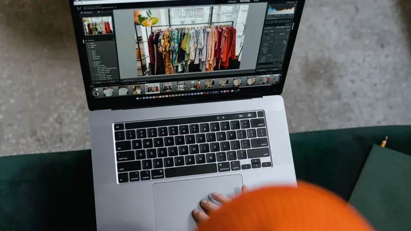 Mains sur un ordinateur portable affichant la retouche d'une photo de portant de vêtements