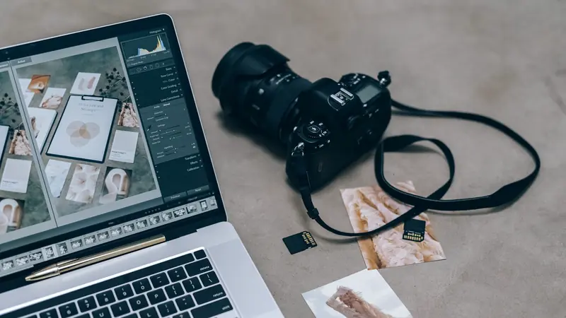 Ordinateur portable ouvert sur un logiciel de retouche photo, à côté d'un appareil reflex, de cartes mémoire et de tirages