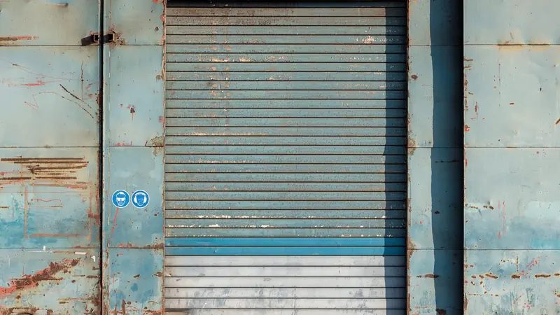 Rideau métallique à lames horizontales, usé et rouillé, sur une façade industrielle bleue