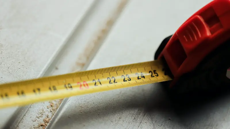 Mètre ruban jaune déroulé sur une planche grise, boîtier rouge au premier plan