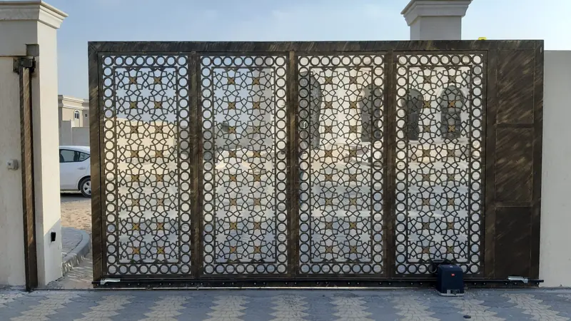Grand portail métallique ajouré à motifs géométriques fermant une entrée pavée
