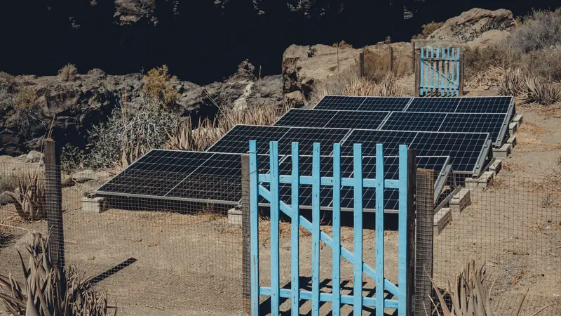 Petit portail bleu devant une rangée de panneaux solaires sur un terrain sec