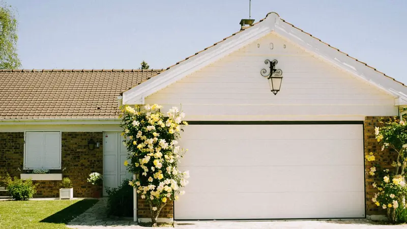 Maison avec une porte de garage blanche encadrée de rosiers en fleurs