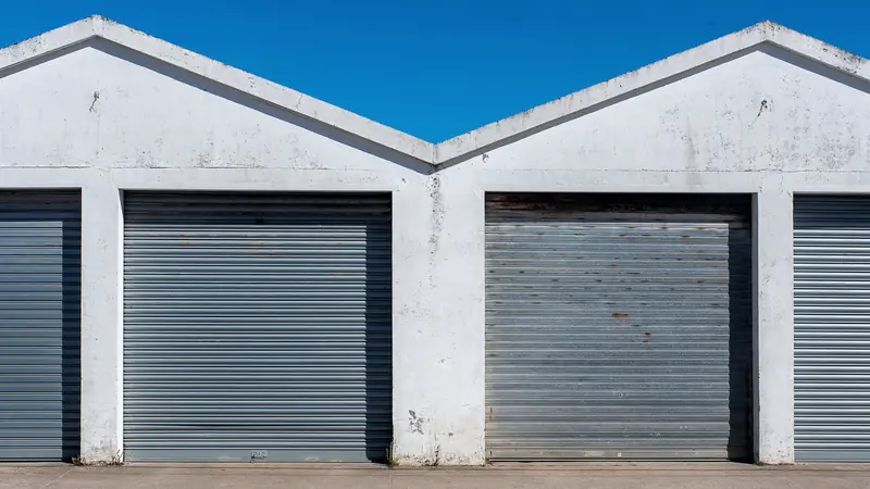 Portes de garage enroulables en acier galvanisé, fermées, dans un bâtiment blanc à pignons