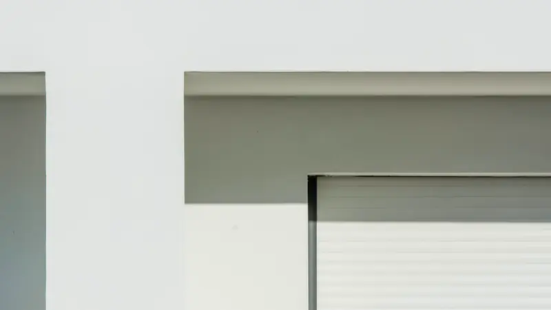 Haut d'une baie avec son linteau en retrait et un tablier à lames blanches dans sa coulisse