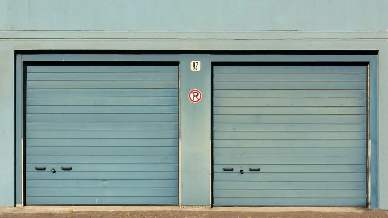 Deux portes de garage métalliques gris-bleu côte à côte dans un mur clair