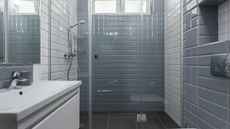 Douche à l'italienne fermée par une paroi vitrée, carrelage métro gris et blanc, lavabo suspendu au premier plan