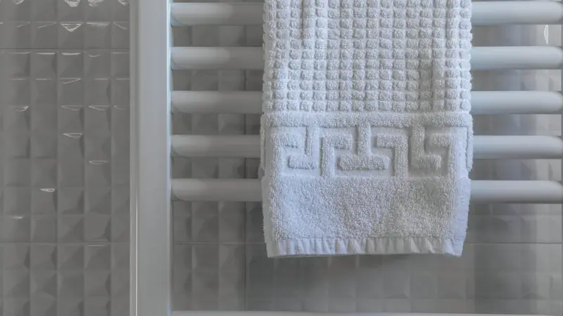 Serviette blanche en éponge posée sur un sèche-serviettes blanc à barreaux devant un mur carrelé