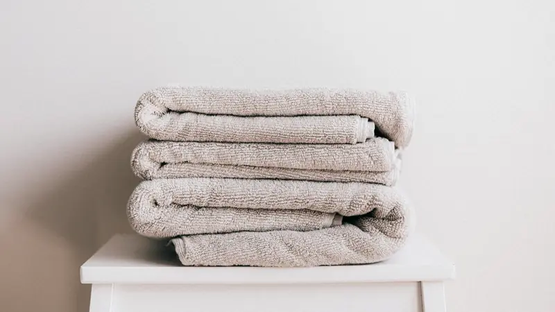 Pile de serviettes éponge beiges pliées sur un tabouret blanc