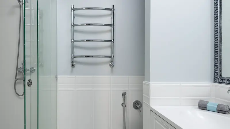 Sèche-serviettes chromé à barreaux fixé au mur entre une douche vitrée et un meuble vasque