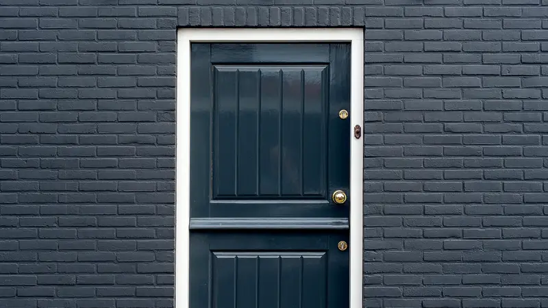 Porte d'entrée noire avec poignée et serrure dans un mur de briques bleu nuit