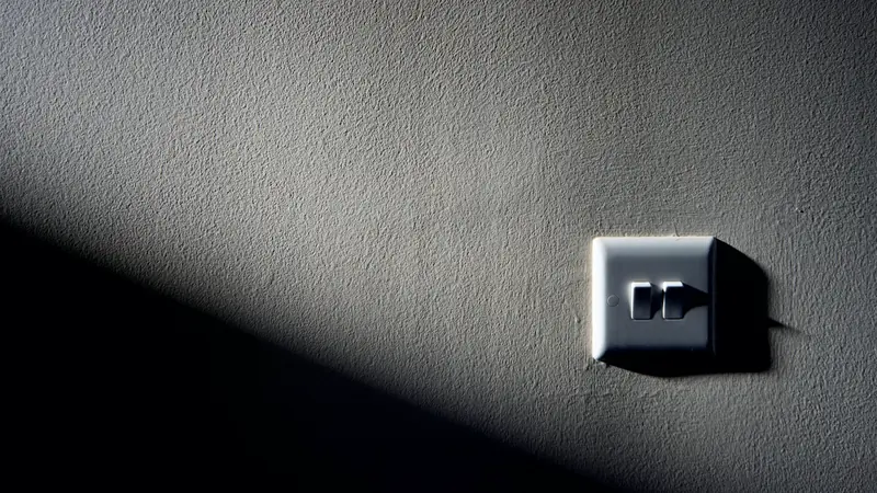Interrupteur mural blanc éclairé par un rai de lumière sur un mur sombre