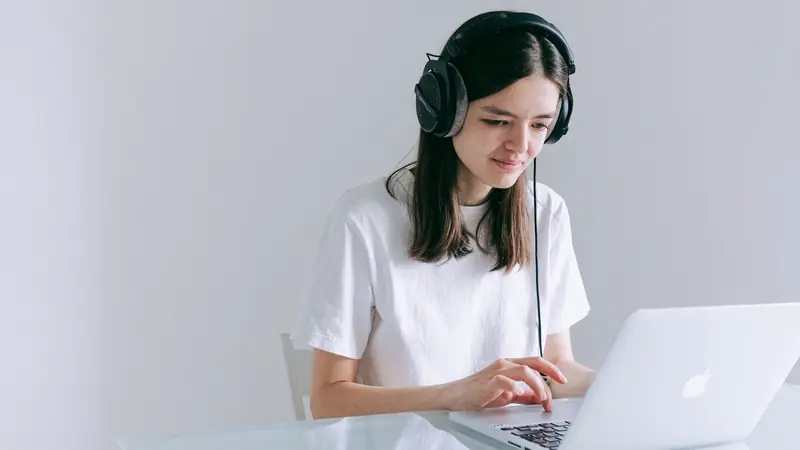 Jeune femme portant un casque audio filaire qui tape sur un ordinateur portable